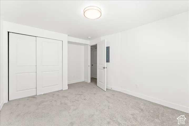 Unfurnished bedroom with light carpet, a closet, and electric panel