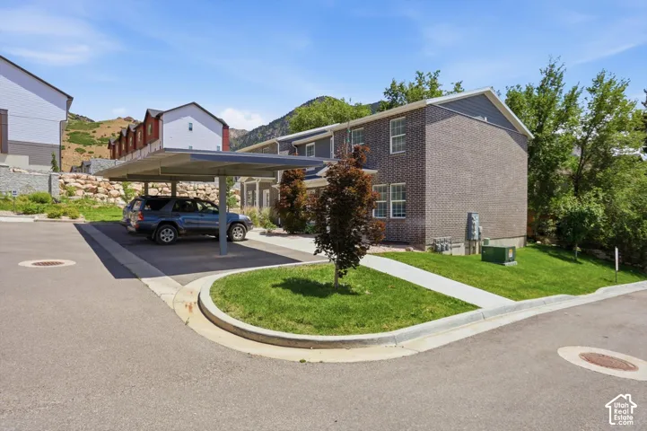 Brick exterior building featuring a covered carport, paved driveway, and manicured lawn