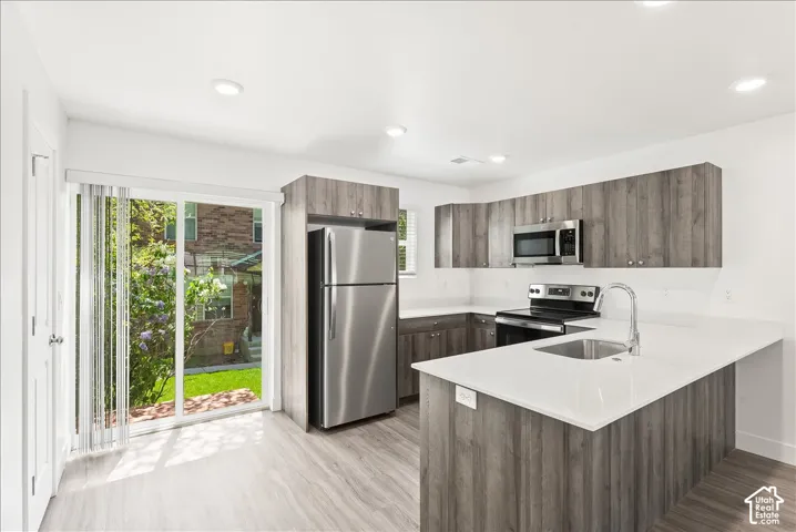 Kitchen with stainless steel appliances, a peninsula, modern cabinets, light stone countertops, and light wood-type flooring