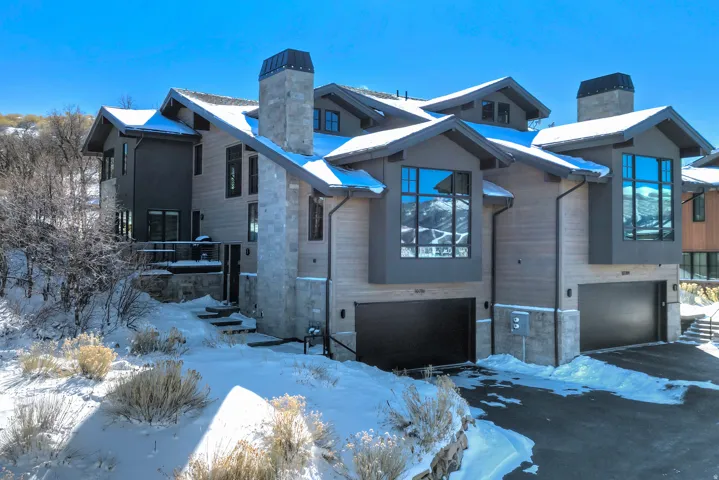 View of front of home featuring a chimney, stone siding, an attached garage, and driveway