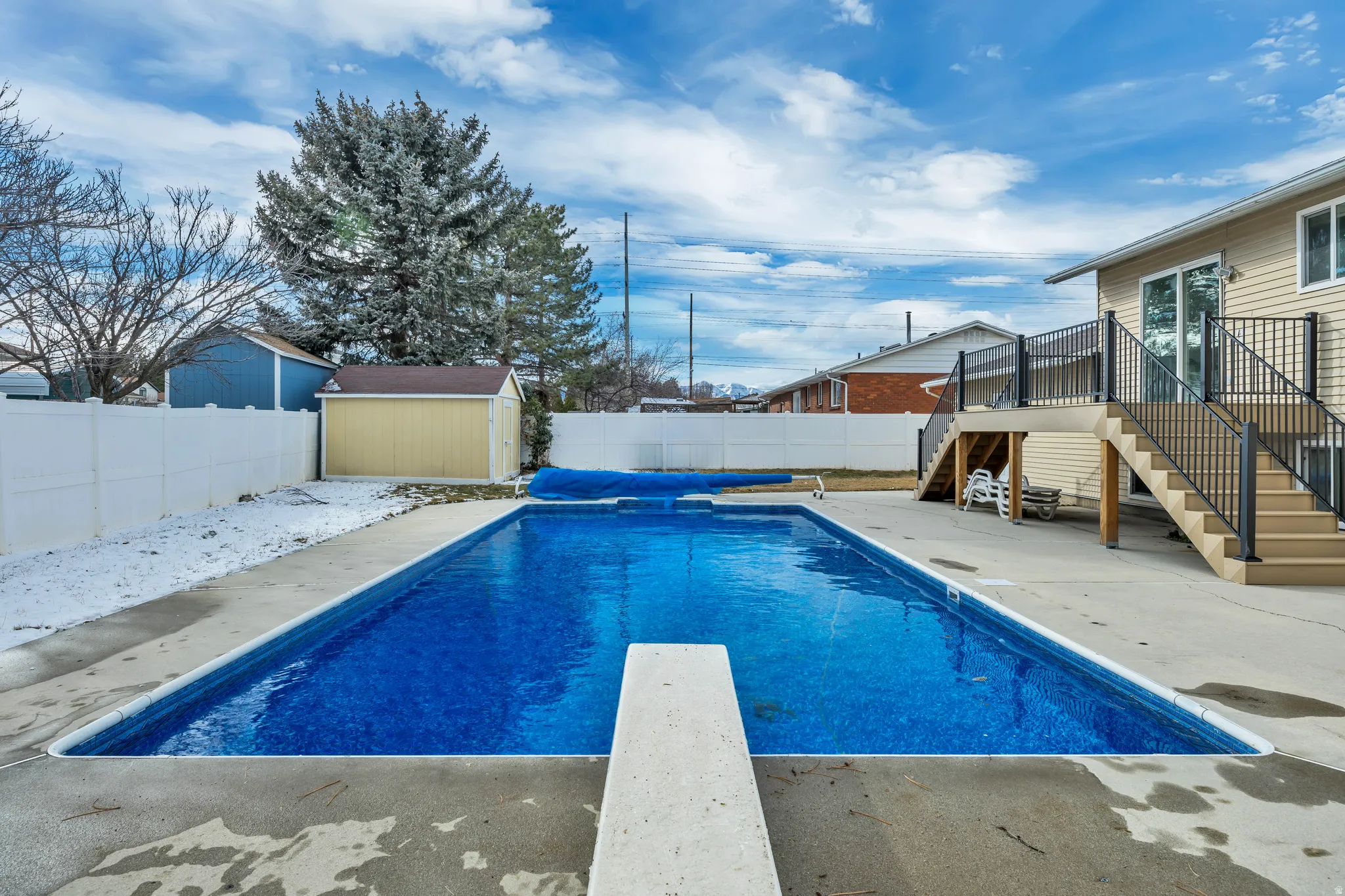View of pool featuring patio surround, a diving board, a fenced backyard, and a wooden deck