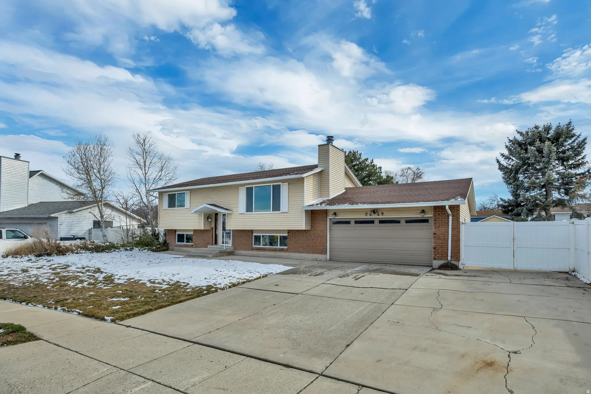 Bi-level home featuring brick siding, a garage, concrete driveway, a chimney, and a gate
