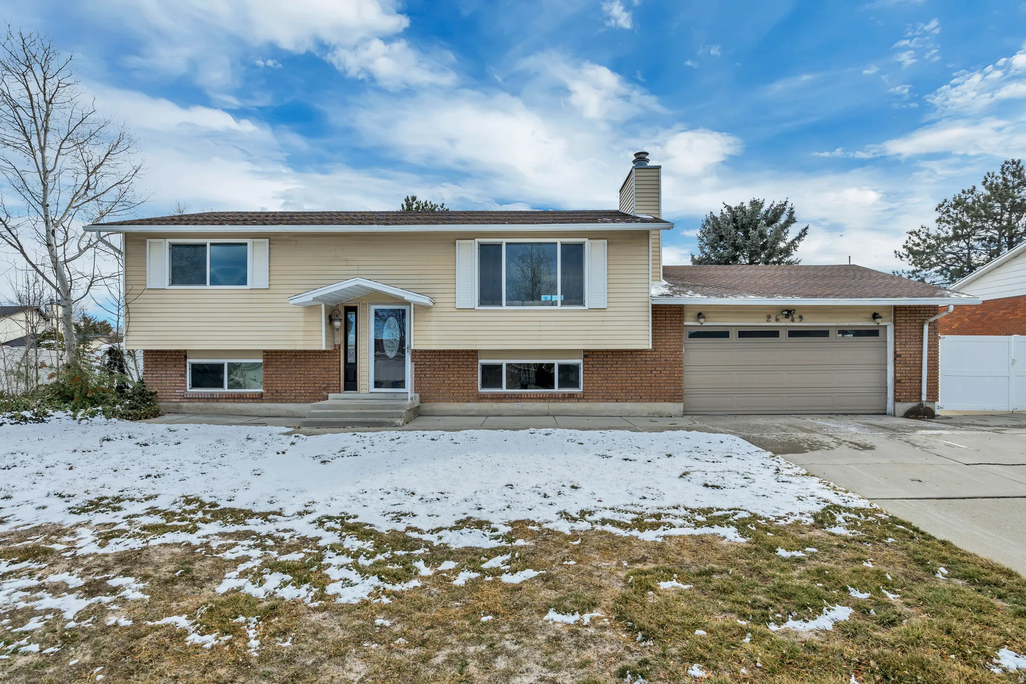 Raised ranch featuring a garage, a chimney, concrete driveway, and brick siding