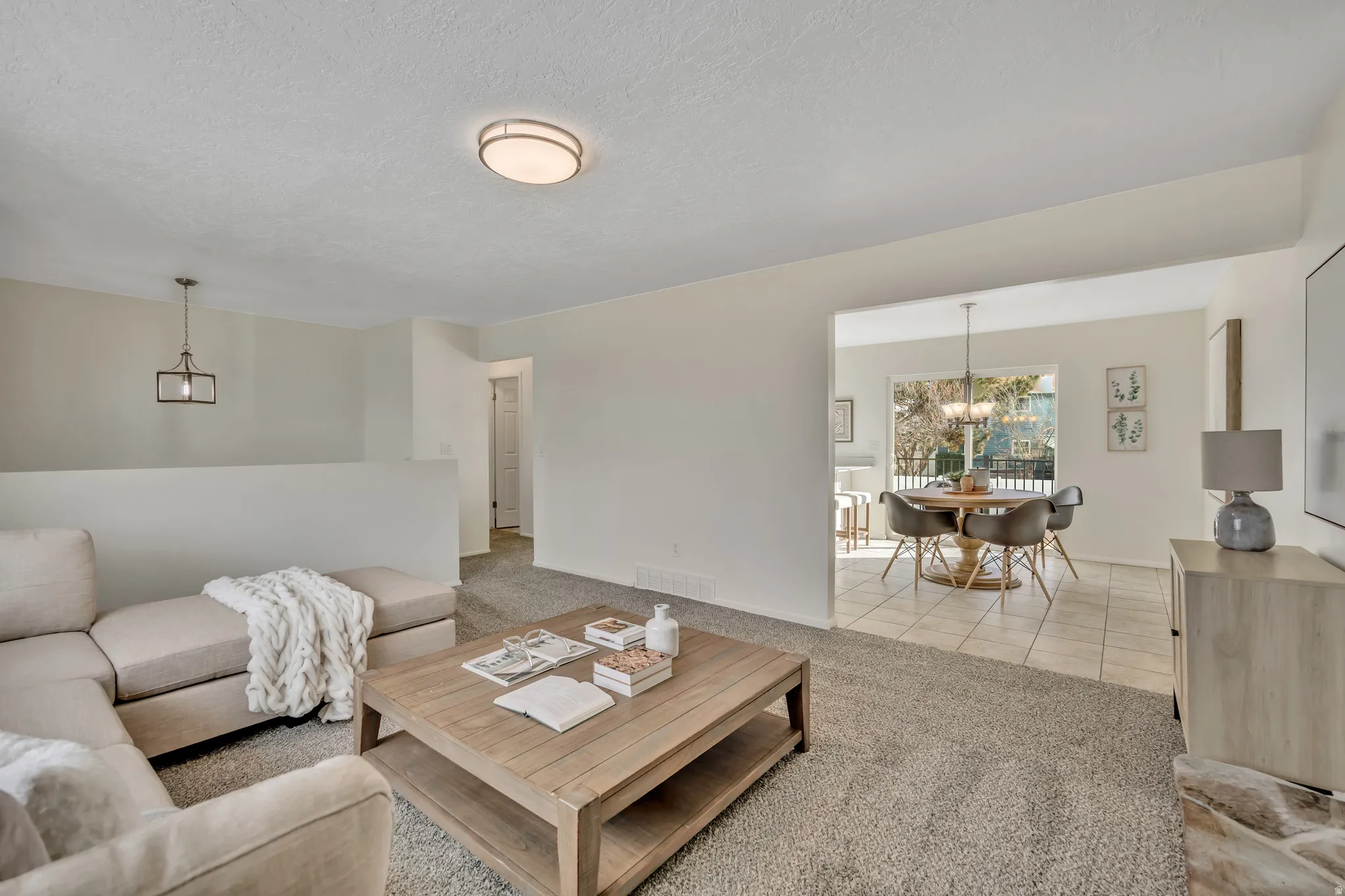 Living room with light colored carpet, light tile patterned floors, a textured ceiling, and hanging lights