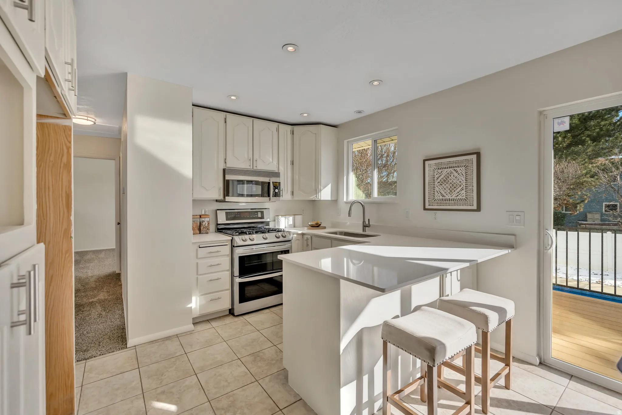 Kitchen featuring a kitchen breakfast bar, a peninsula, stainless steel appliances, light colored carpet, and white cabinets