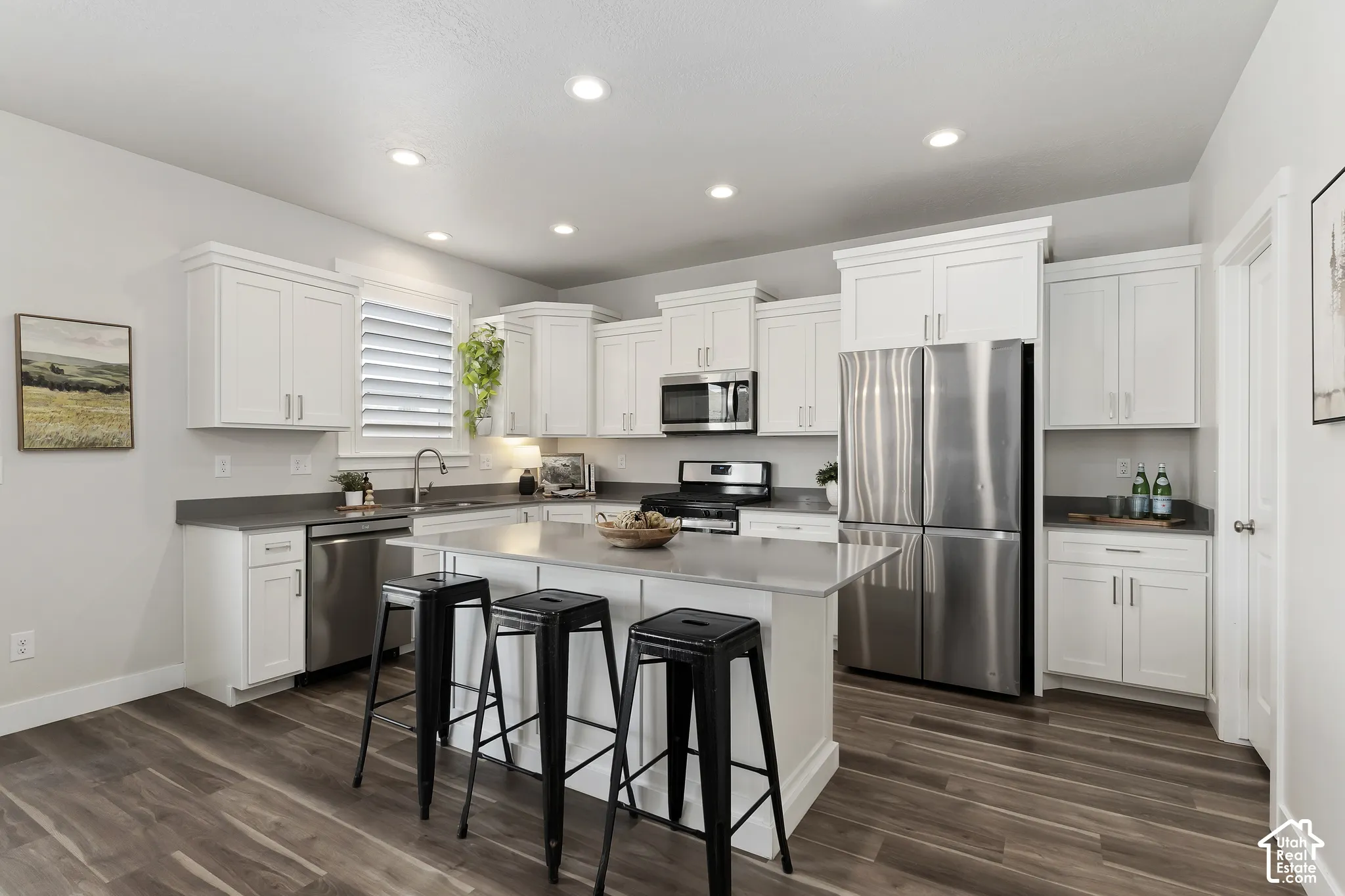 Open kitchen with white cabinetry, granite countertops, stainless steel appliances, oversized island, and walk-in pantry.