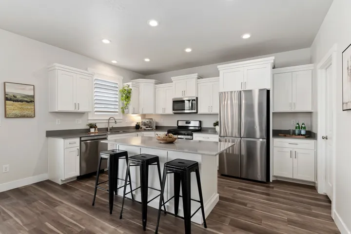 Open kitchen with white cabinetry, granite countertops, stainless steel appliances, oversized island, and walk-in pantry.
