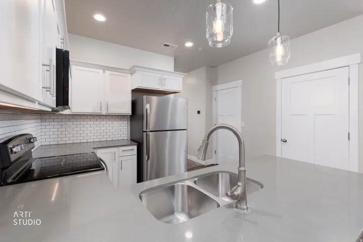 Kitchen with freestanding refrigerator, range with electric stovetop, decorative light fixtures, white cabinets, and light stone counters