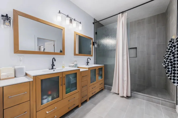 Bathroom featuring two vanities, a shower stall, and light tile patterned flooring