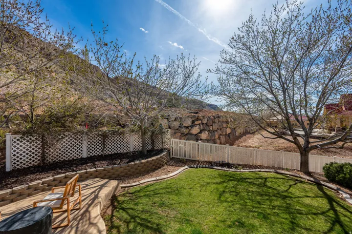 Tiered backyard featuring a manicured lawn, concrete patio, and white lattice fencing