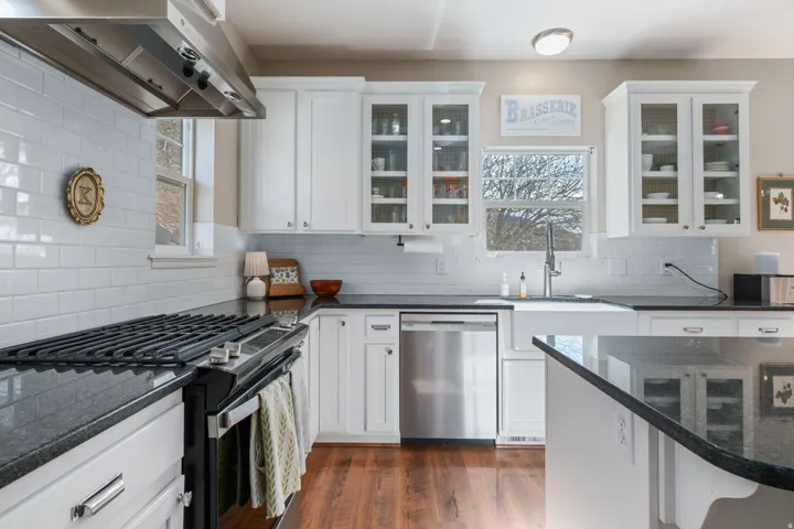 Kitchen featuring range with gas cooktop, dark stone counters, stainless steel dishwasher, white cabinets, and glass fronted cabinets