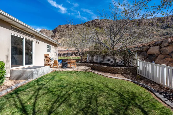Sliding glass door access to a patio with stone pavers, bordered by a retaining wall, a white lattice fence, and a white picket fence