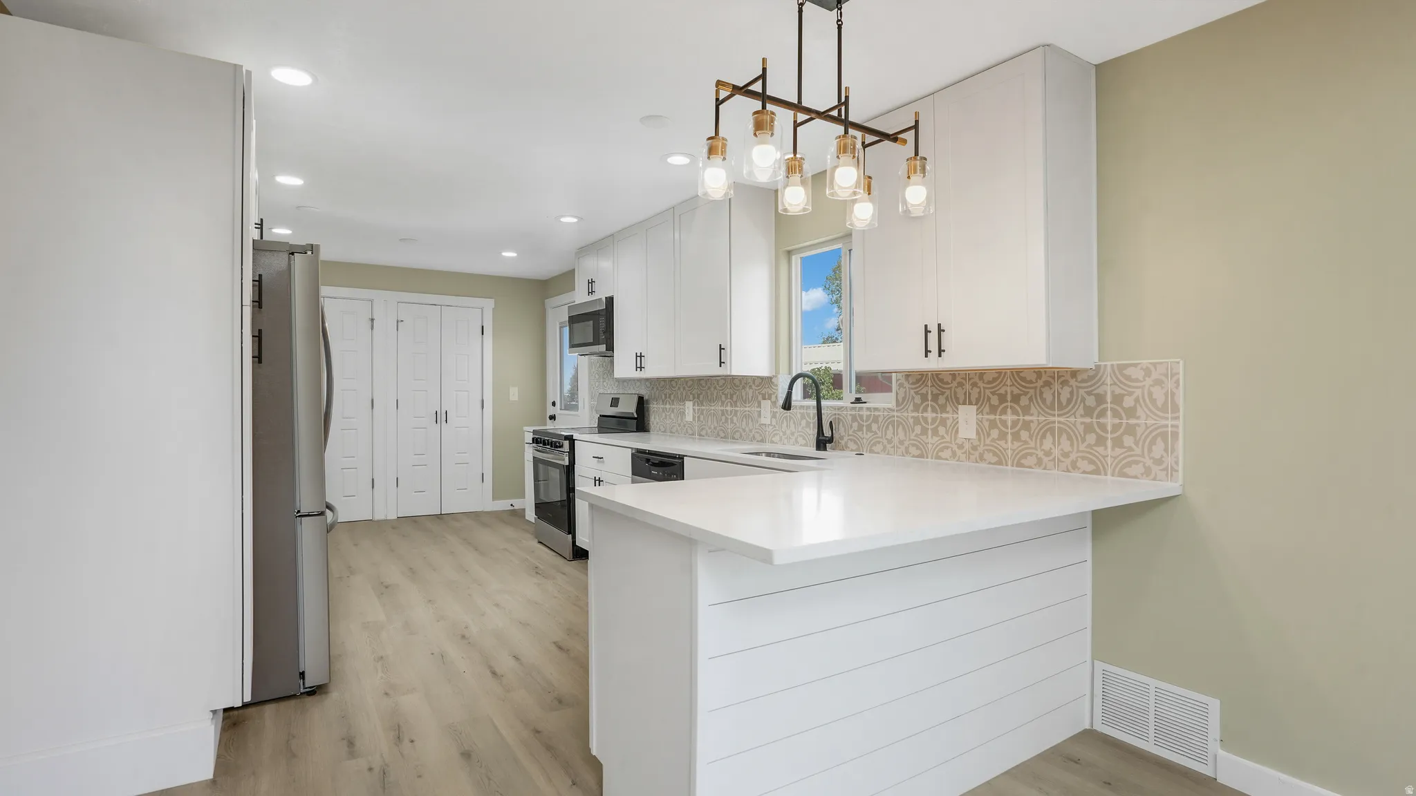 Kitchen with a peninsula, white cabinetry, light wood-type flooring, and stainless steel appliances