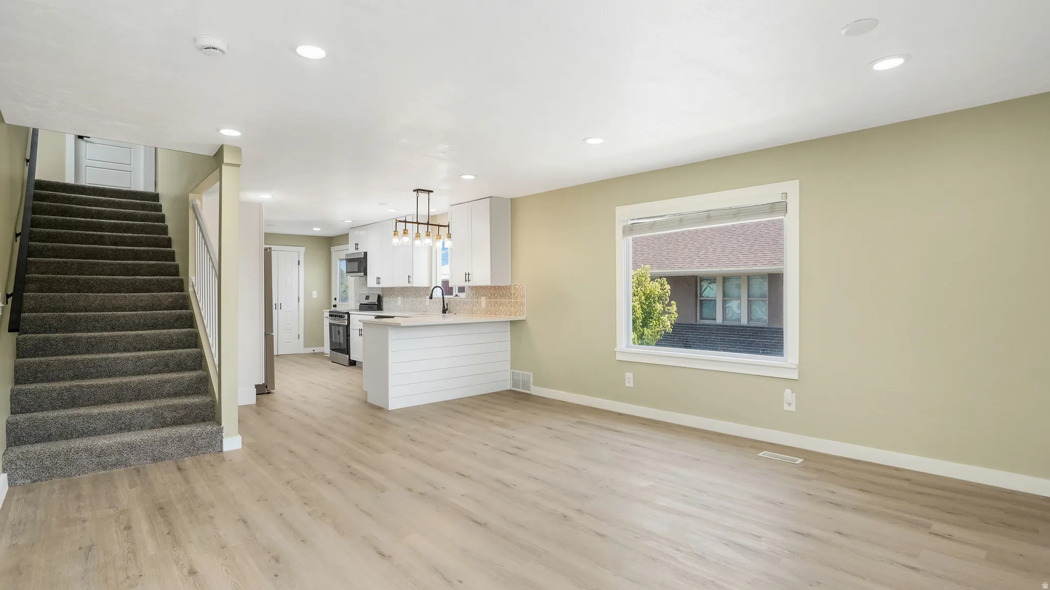 Kitchen with a peninsula, light wood-style flooring, pendant lighting, stainless steel appliances, and tasteful backsplash