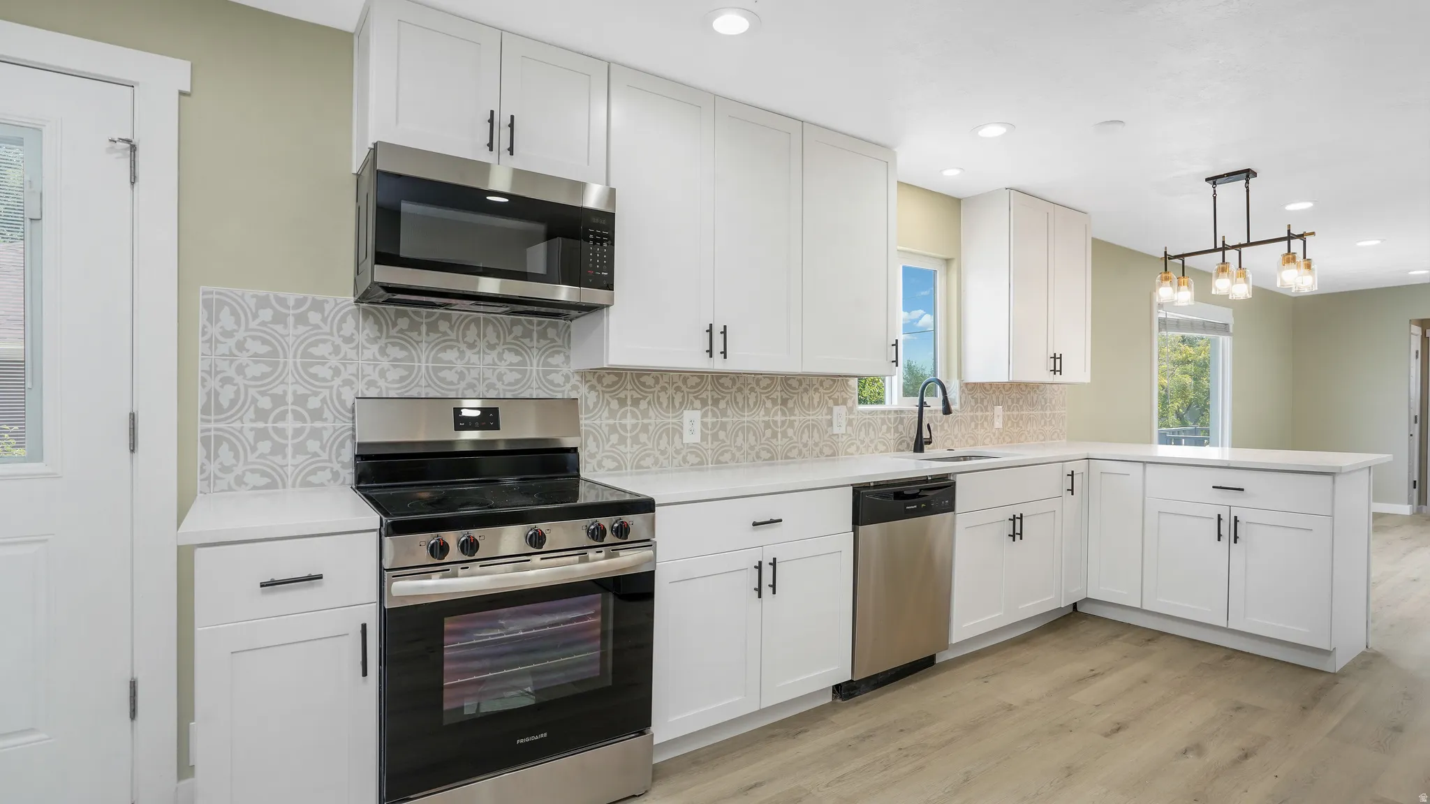 Kitchen with stainless steel appliances, decorative backsplash, light wood finished floors, a peninsula, and hanging light fixtures
