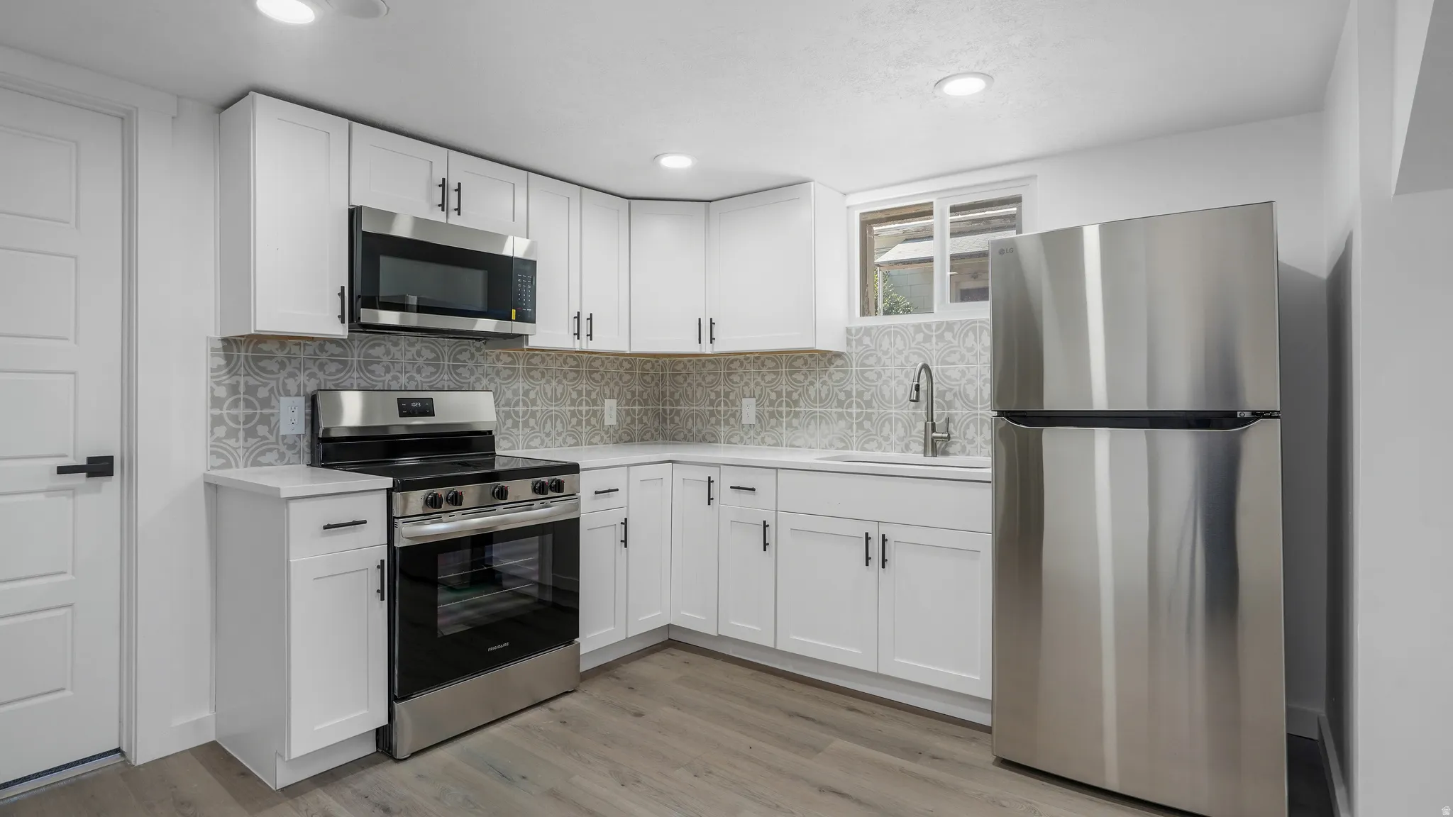 Kitchen with stainless steel appliances, white cabinets, decorative backsplash, and light wood-style floors