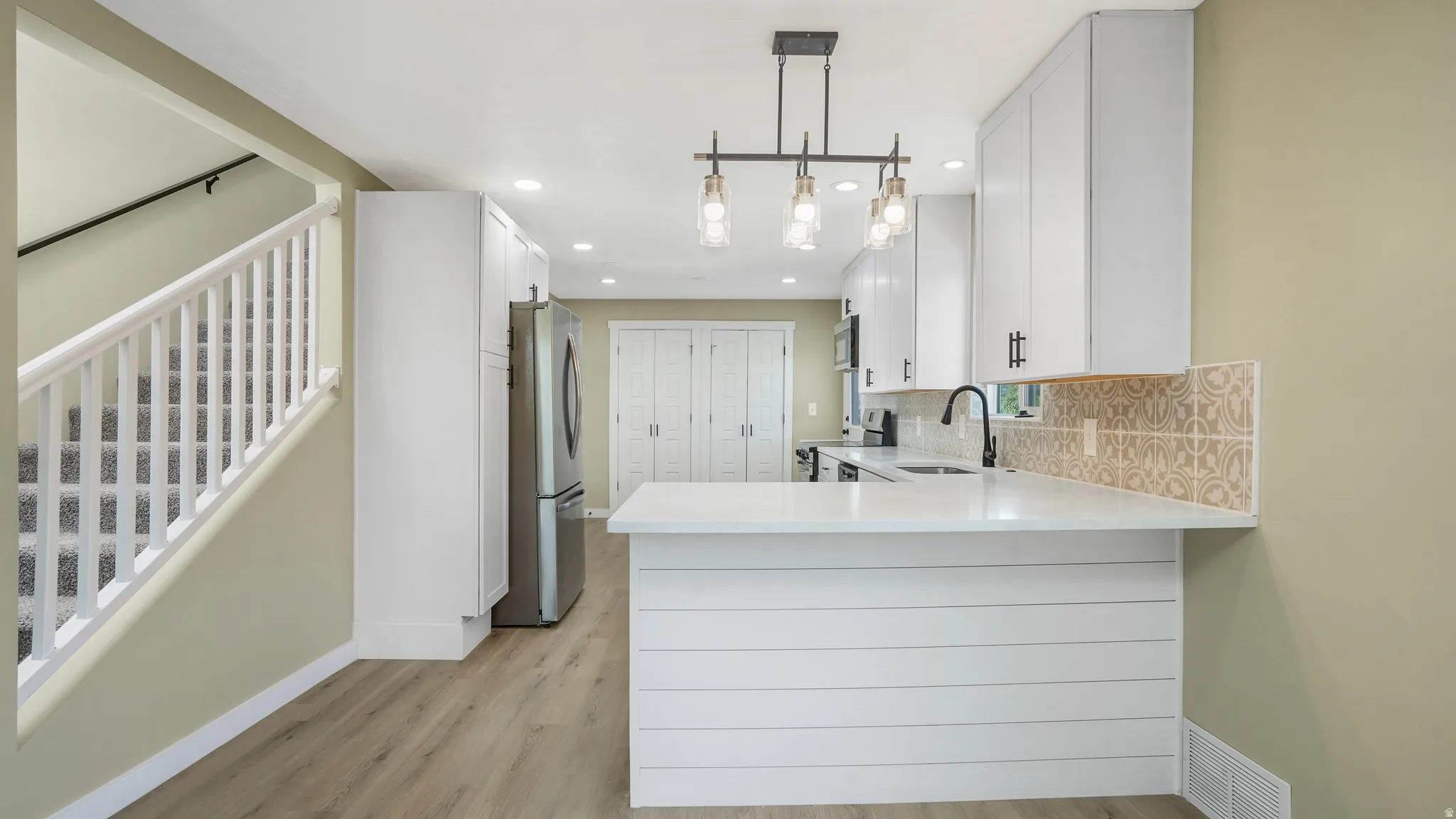 Kitchen featuring white cabinetry, stainless steel appliances, light stone counters, and a peninsula