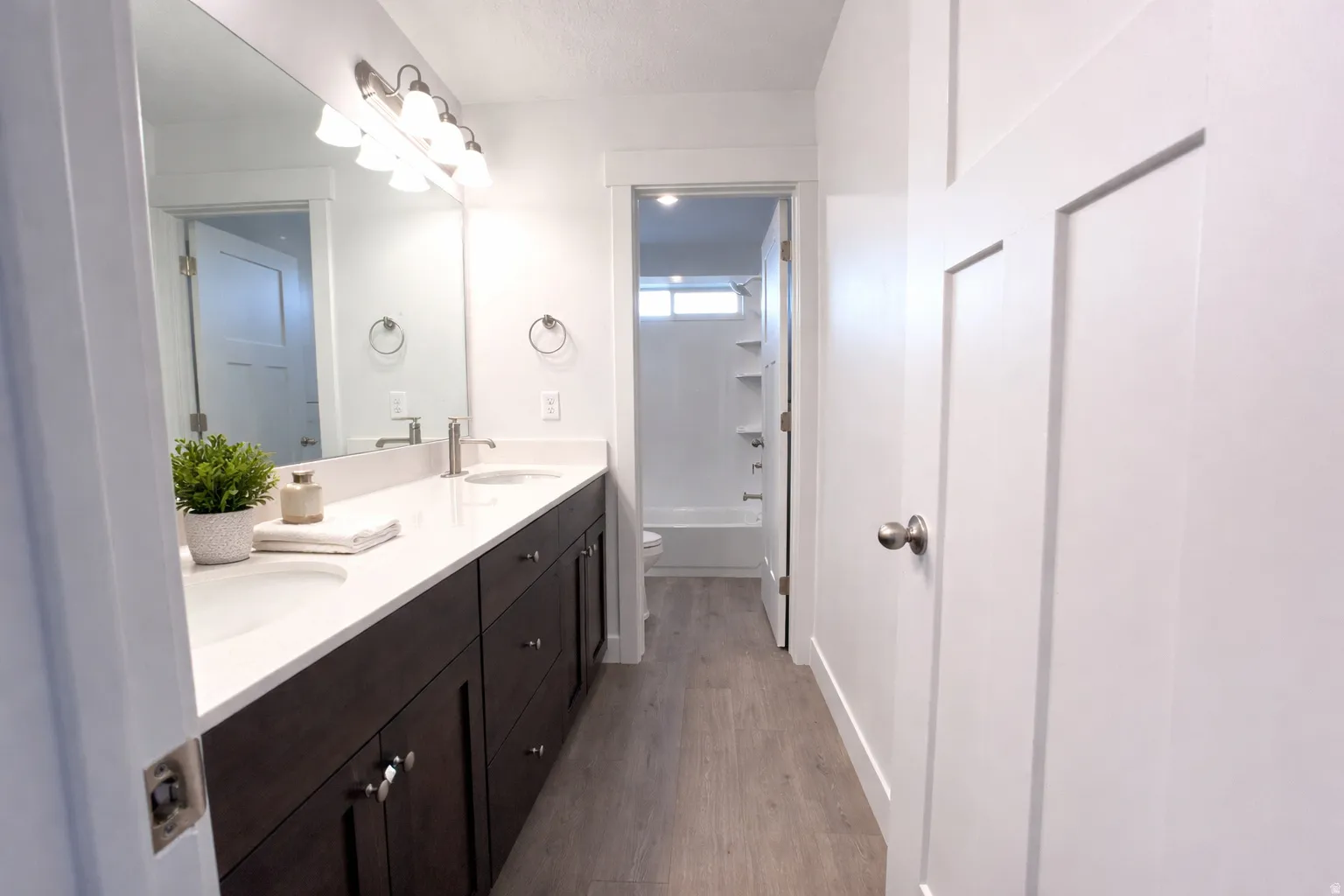 Full bathroom featuring double vanity, dark wood-style flooring, and shower / bath combination