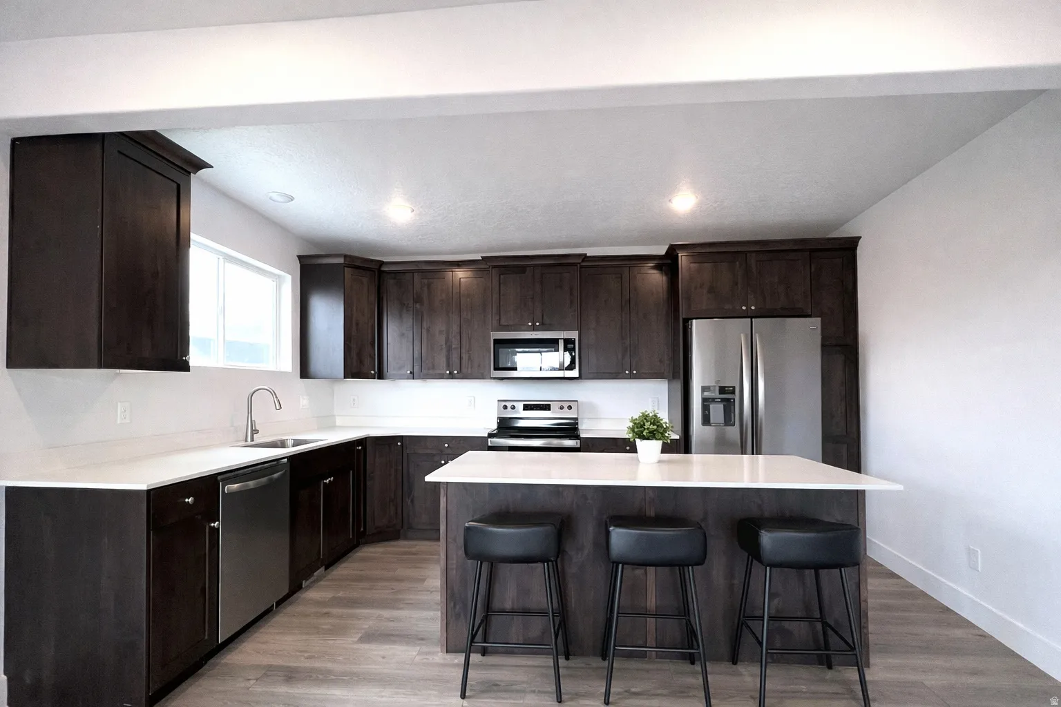 Kitchen with dark wood finish cabinetry, stainless steel appliances, light wood finished floors, a kitchen island, and a kitchen bar