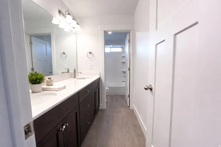 Full bathroom featuring double vanity, dark wood-style flooring, and shower / bath combination