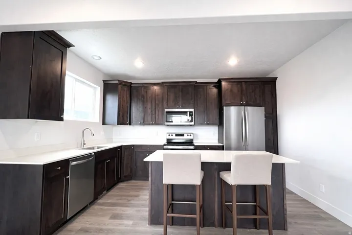 Kitchen with dark wood finish cabinets, stainless steel appliances, a kitchen island, light wood-type flooring, and recessed lighting