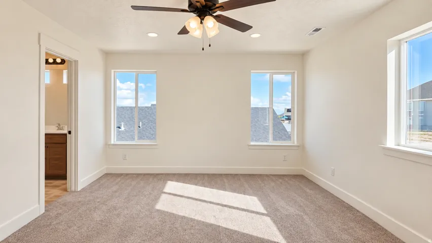 Recessed lighting, ceiling fan with light fixture, multiple windows, carpet flooring, and an adjoining bathroom with wood-finish vanity