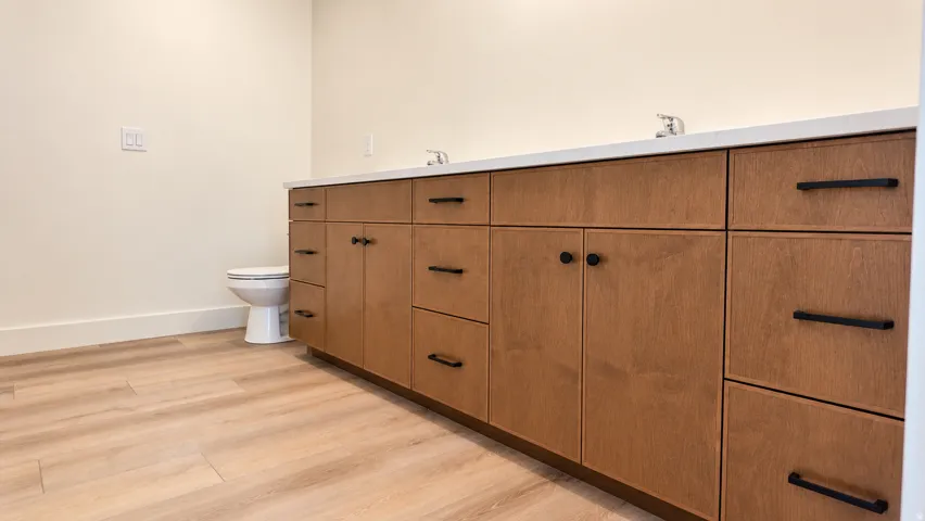 Dual-sink vanity with wood-finish cabinetry, matte black hardware, and light-toned countertop
