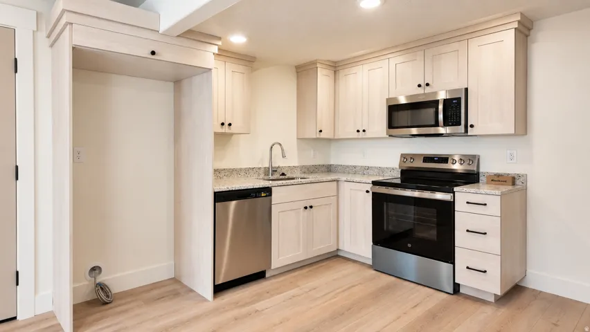 Kitchen featuring light wood-finish cabinetry, stainless steel appliances, granite countertops, and wood-finish flooring