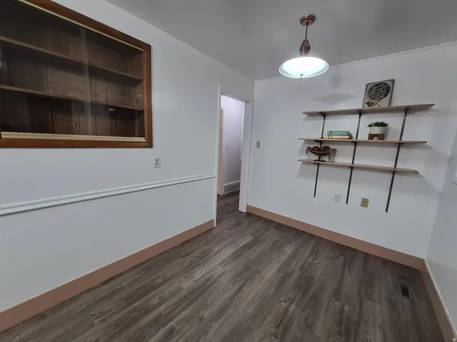 Unfurnished dining area featuring dark wood-type flooring and baseboards