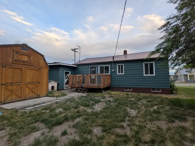 Rear exterior showcasing a wood deck with railing, stepping stones, and a detached wooden shed