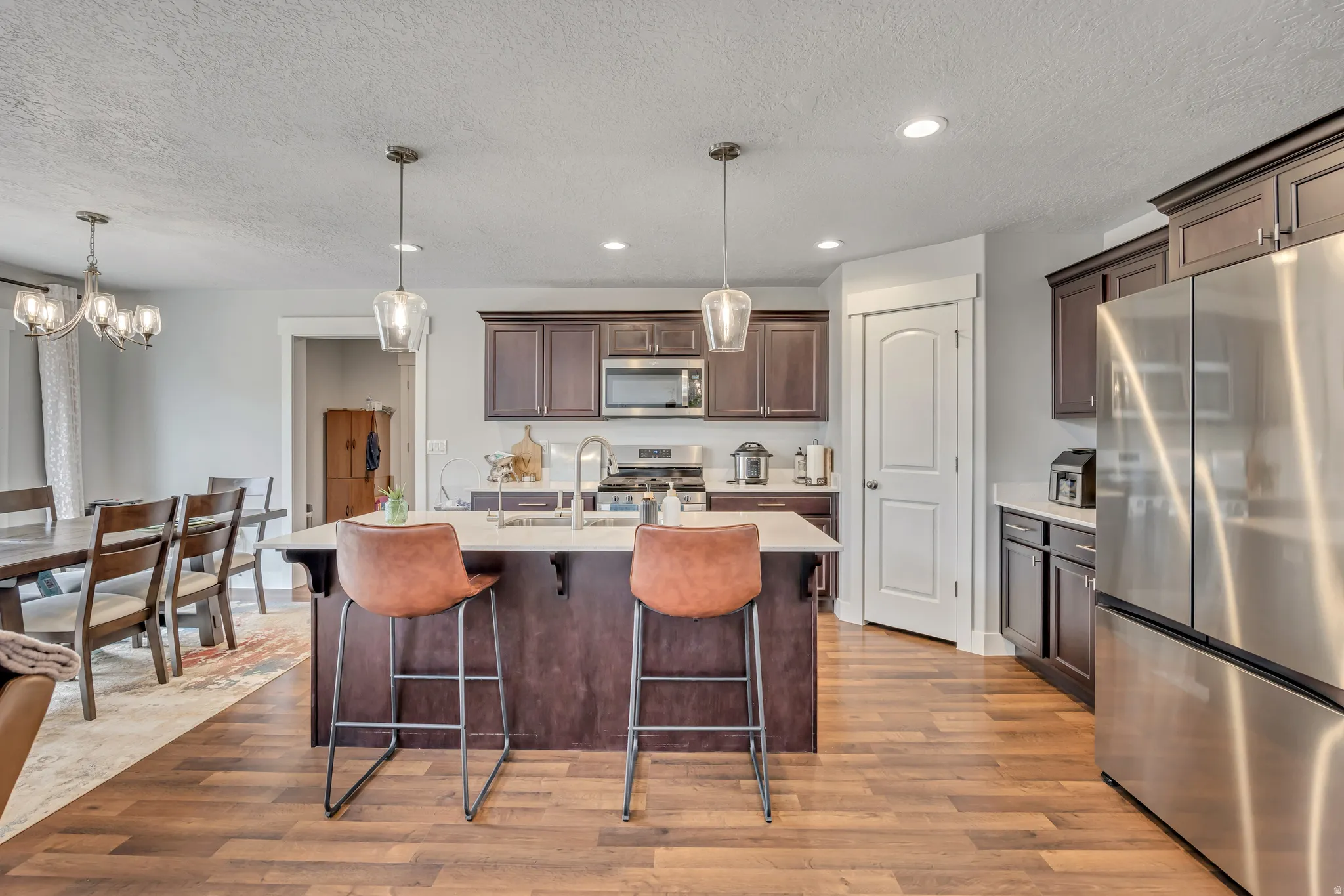 Kitchen with dark wood finish cabinetry, stainless steel appliances, a kitchen breakfast bar, hanging lights, and a textured ceiling