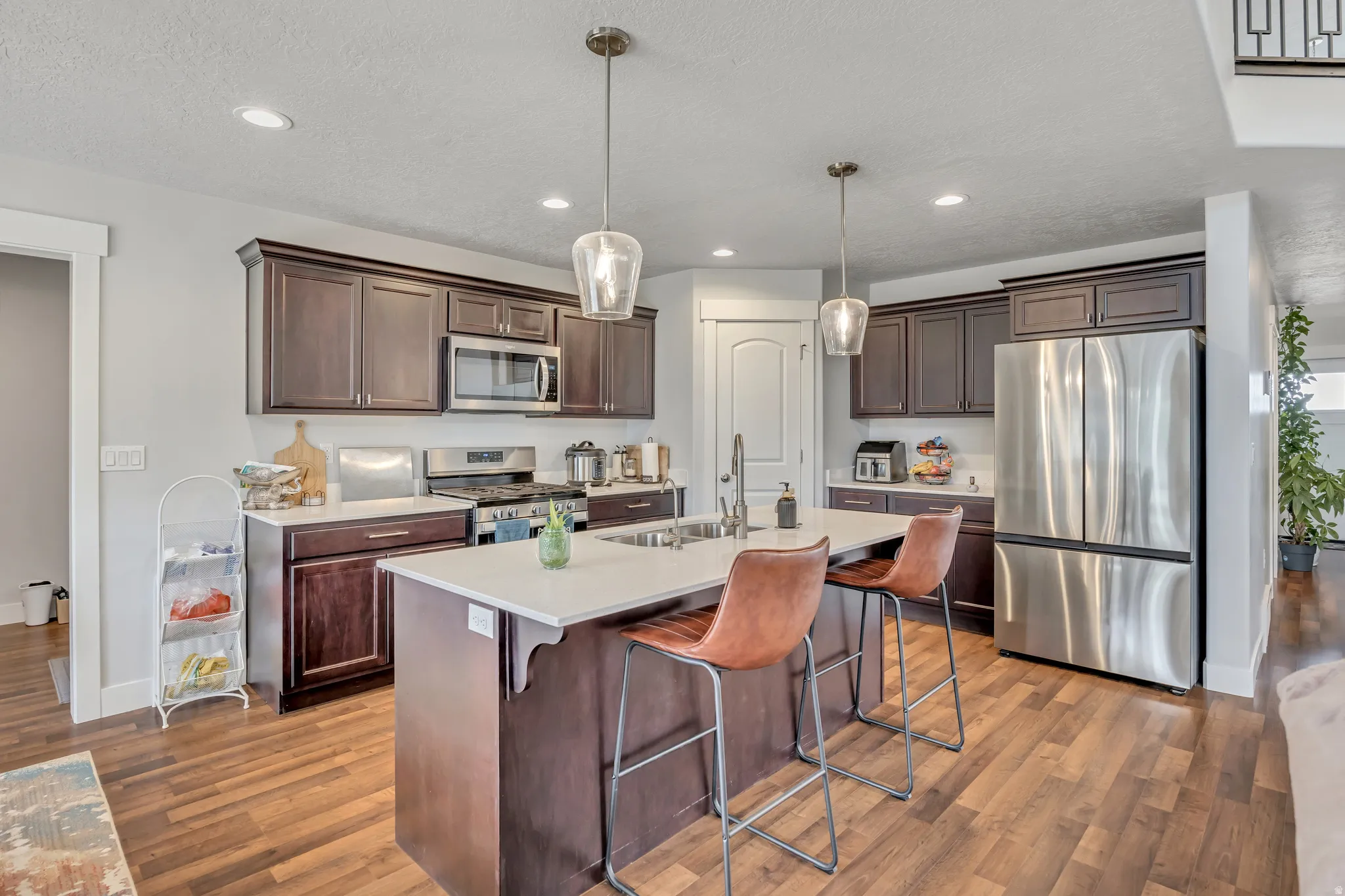 Kitchen featuring a breakfast bar, stainless steel appliances, a center island with sink, dark wood finish cabinets, and a textured ceiling
