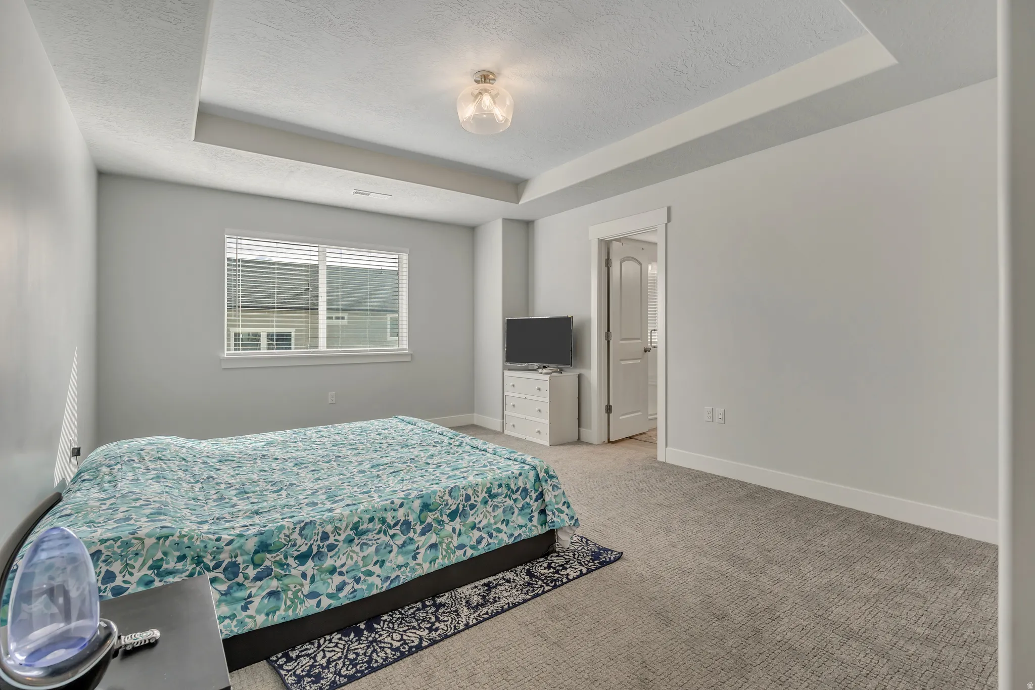 Bedroom with a tray ceiling, light colored carpet, and a textured ceiling