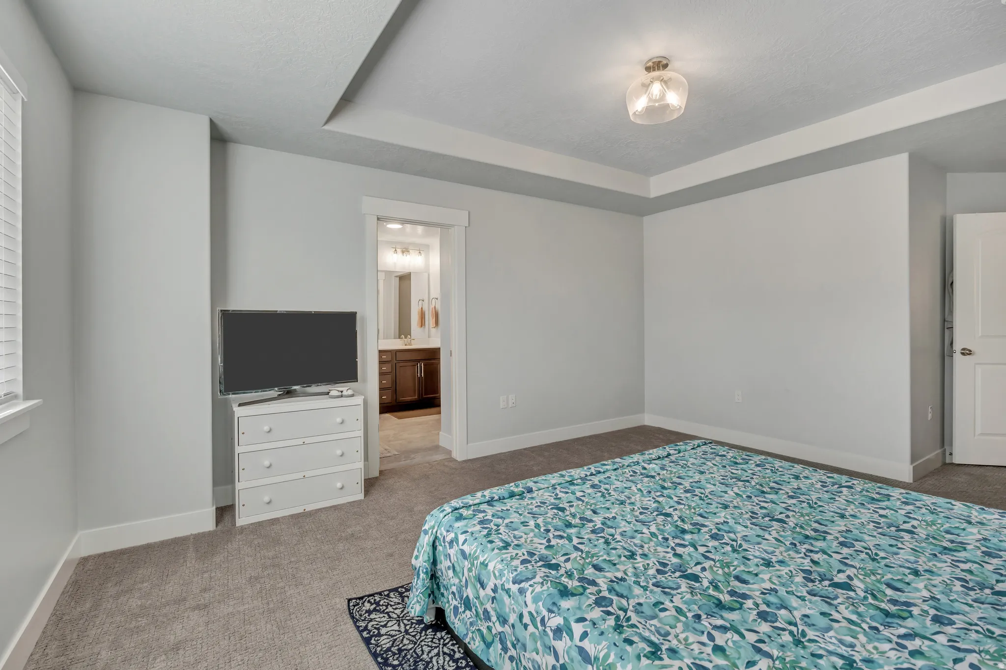 Bedroom with light carpet, a raised ceiling, ensuite bath, and a textured ceiling