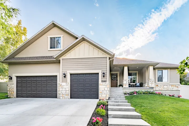View of front facade with stone siding, covered porch, and concrete driveway