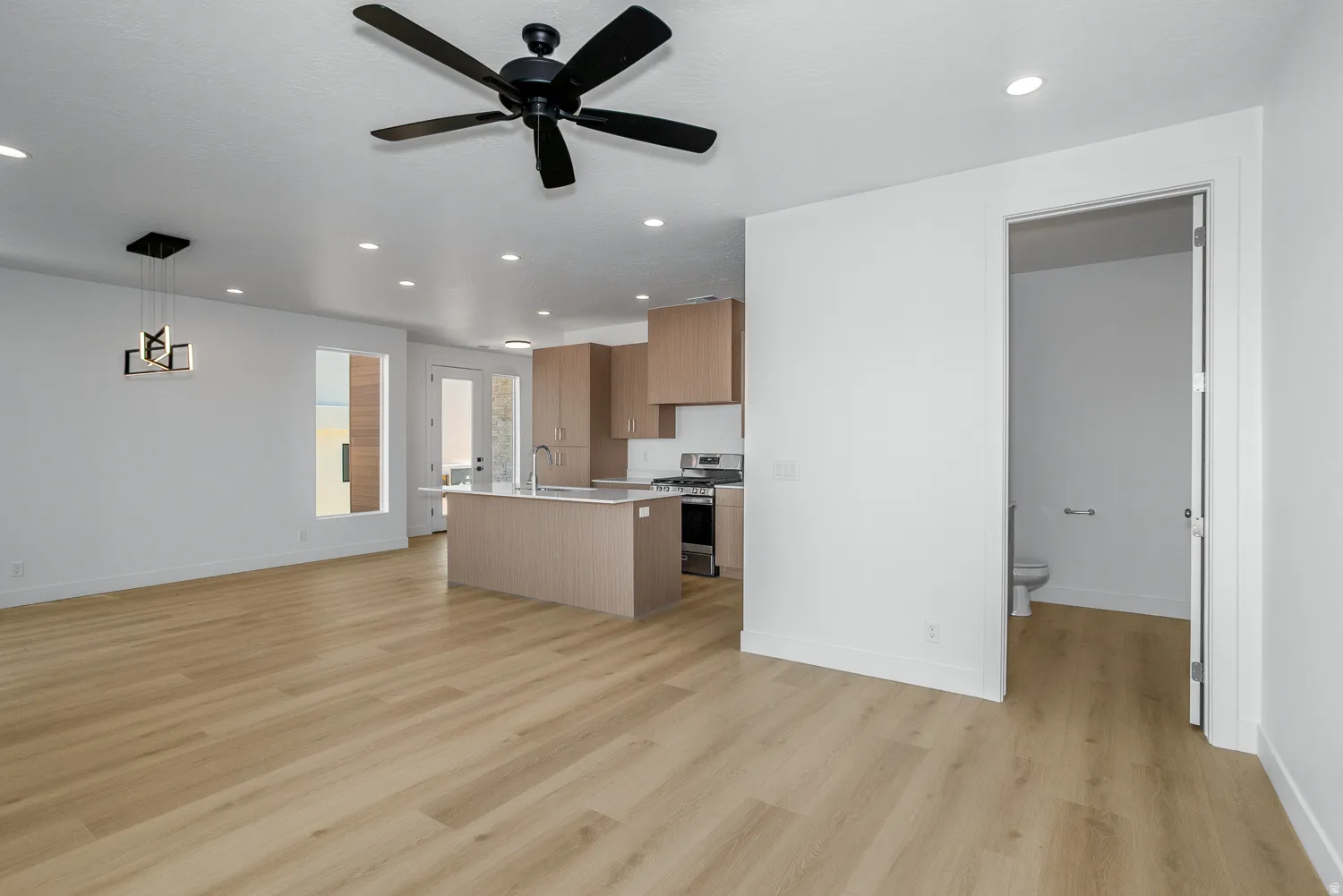 Kitchen with open floor plan, stainless steel gas stove, a kitchen island with sink, a ceiling fan, and light wood-style flooring