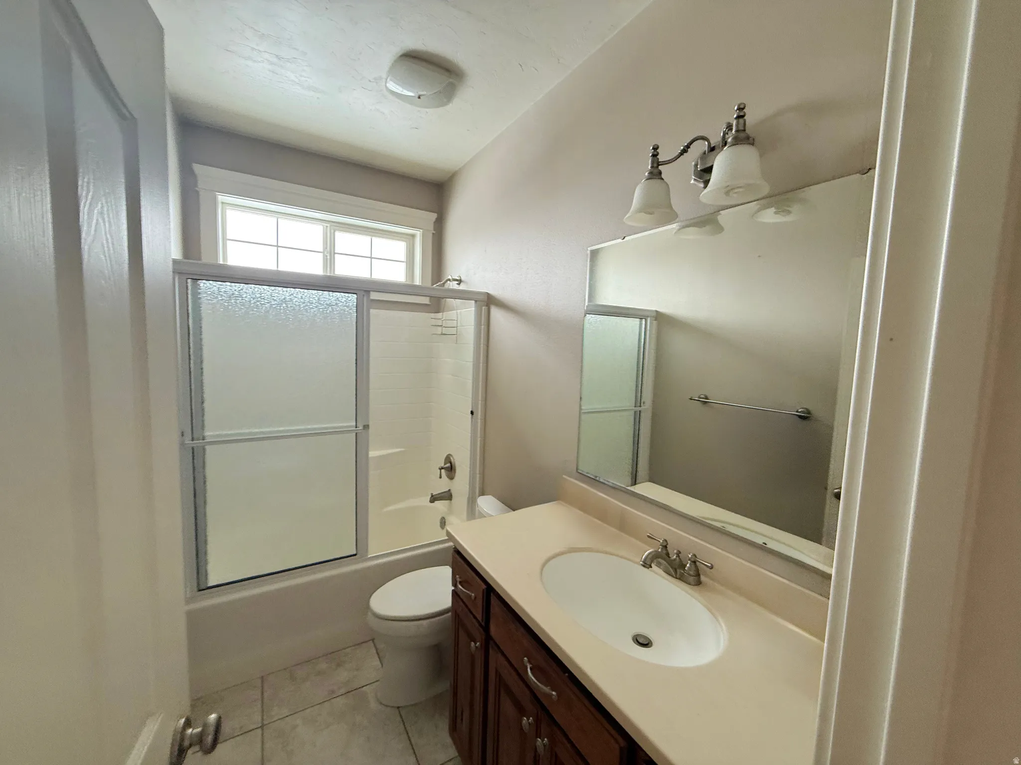 Bathroom with combined bath / shower with glass door, vanity, and light tile patterned flooring