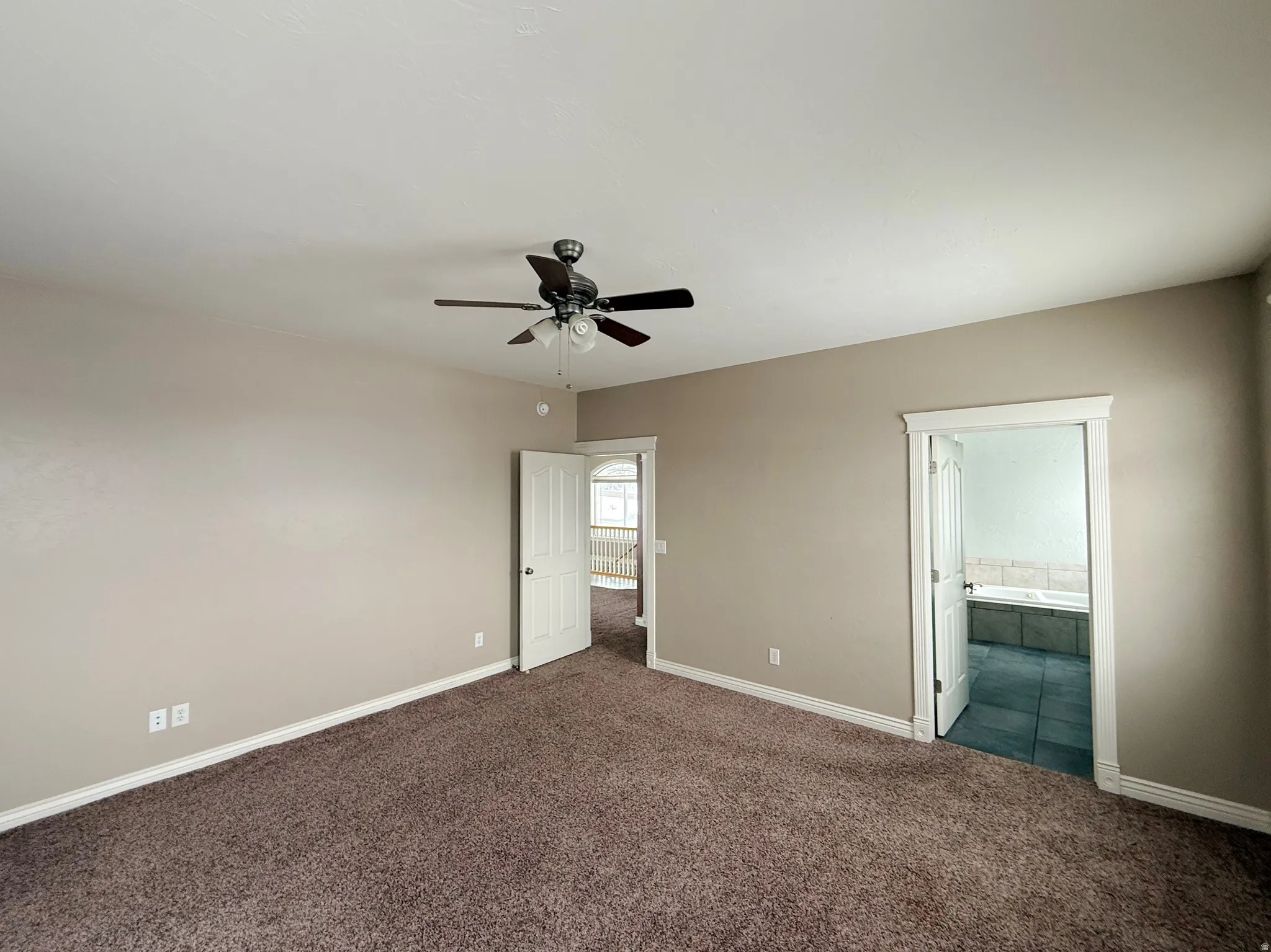 Unfurnished bedroom with dark colored carpet, ceiling fan, and connected bathroom