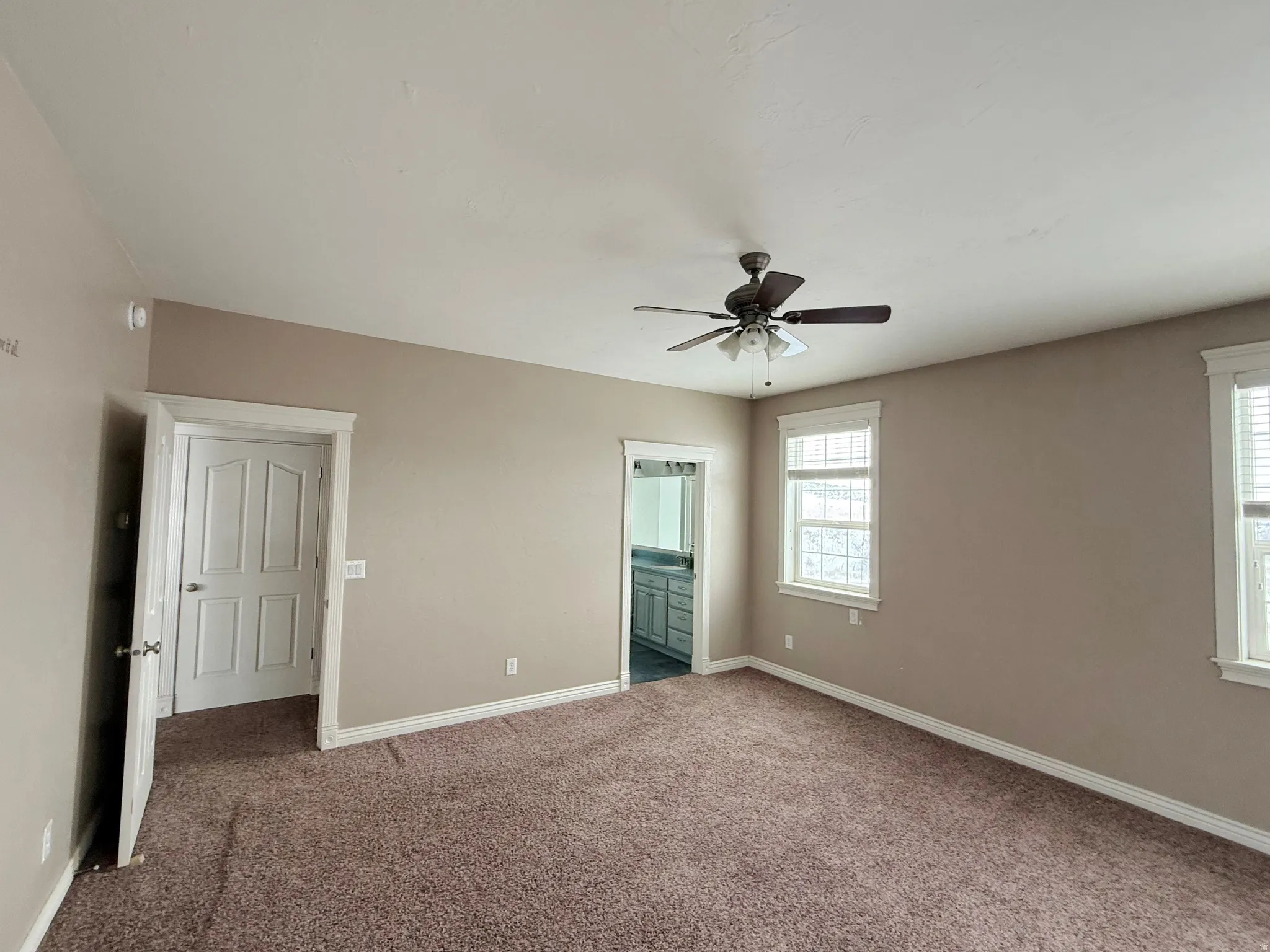 Unfurnished bedroom featuring ensuite bath, dark colored carpet, and ceiling fan
