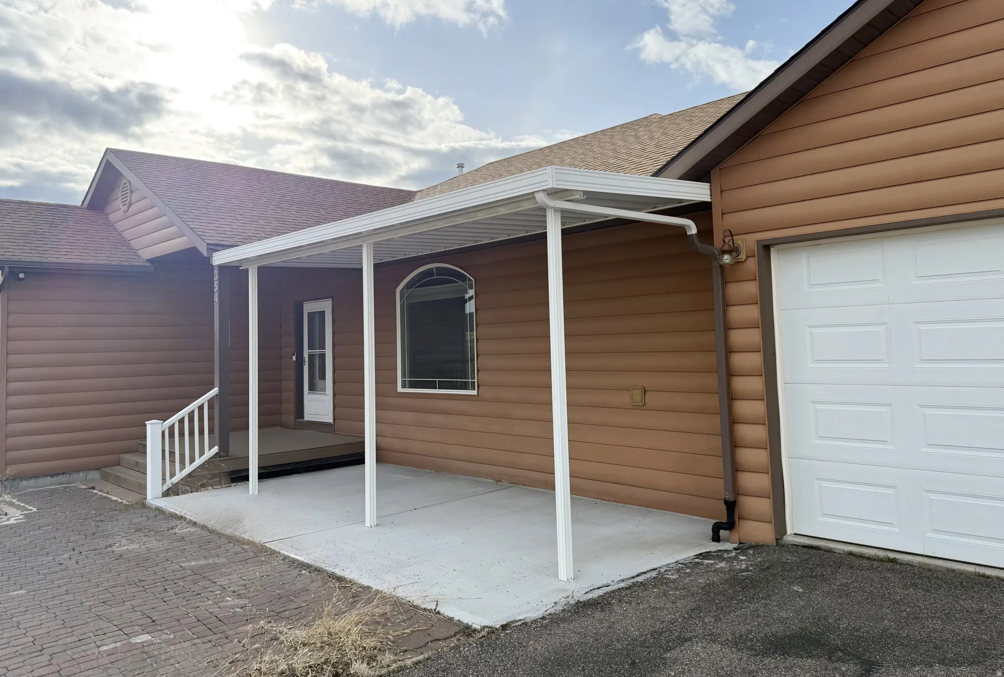 Doorway to property with roof with shingles, a patio area, faux log siding, and a garage