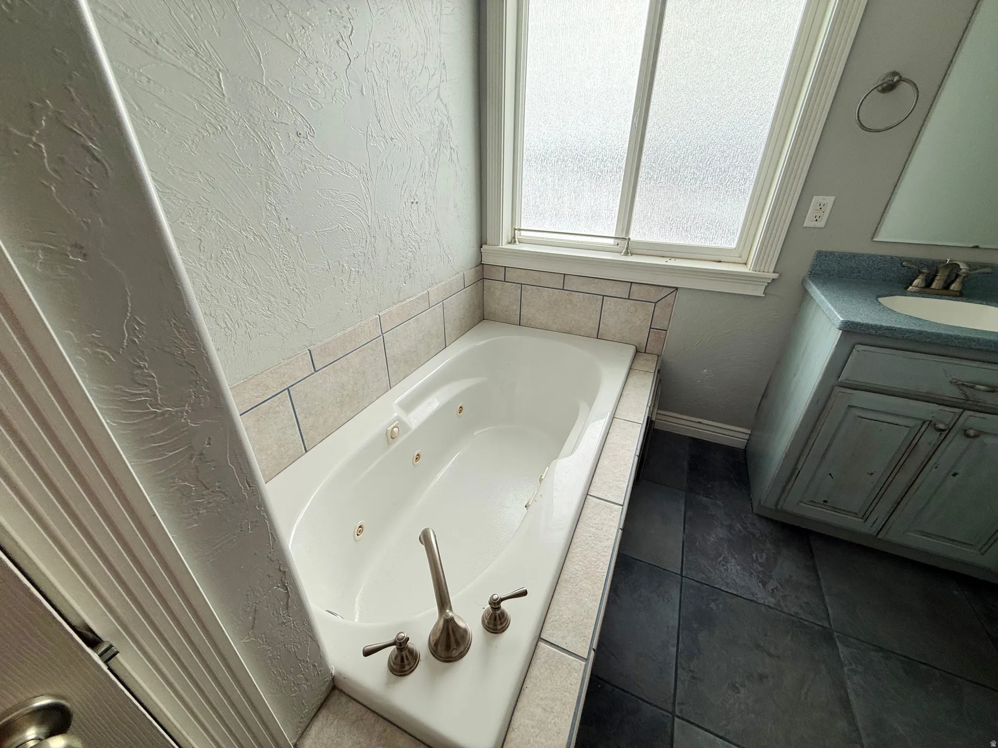 Full bath with a textured wall, a tub with jets, and vanity