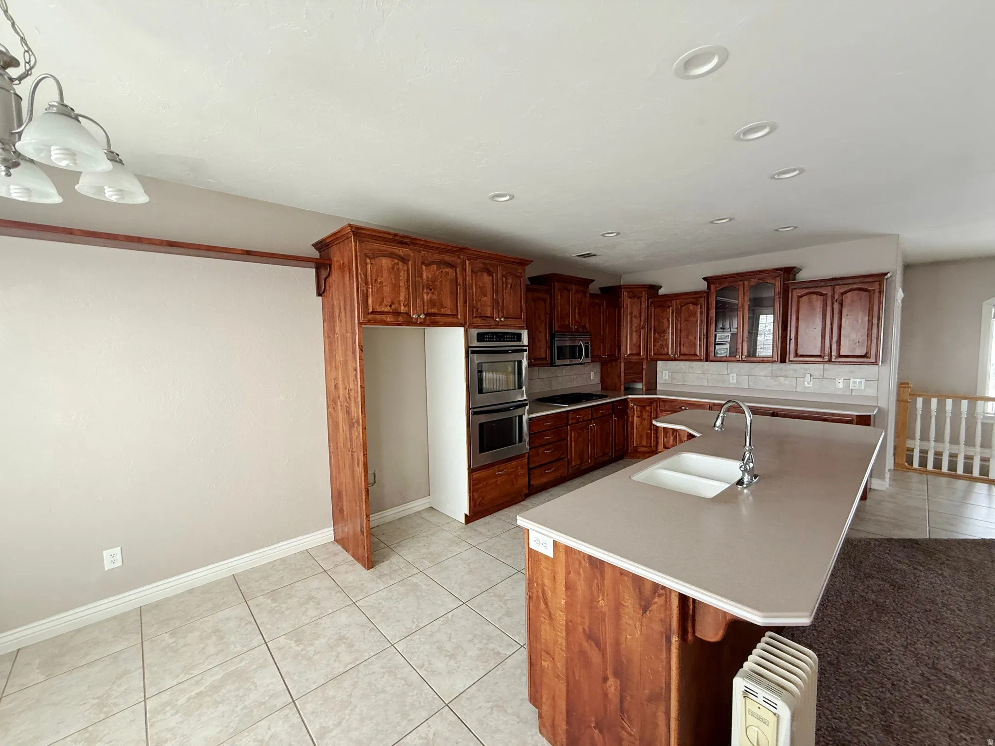 Kitchen with light tile patterned floors, a kitchen island with sink, light countertops, decorative backsplash, and stainless steel appliances