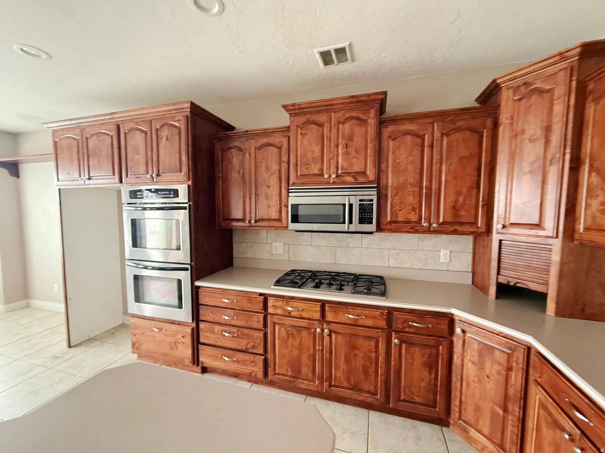 Kitchen featuring wood finish cabinets, light tile patterned floors, stainless steel appliances, and recessed lighting