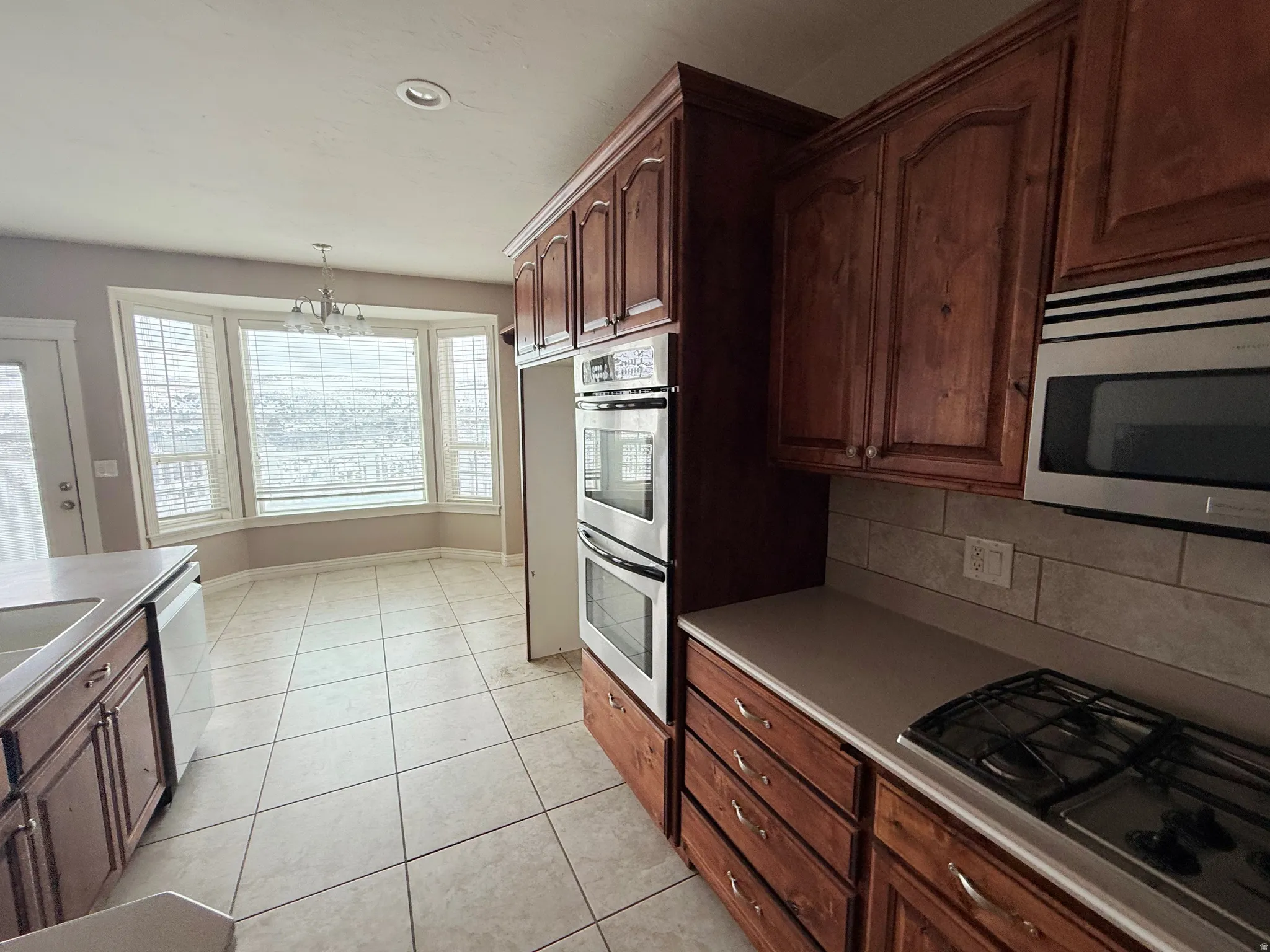 Kitchen with stainless steel appliances, a chandelier, backsplash, light tile patterned floors, and light countertops