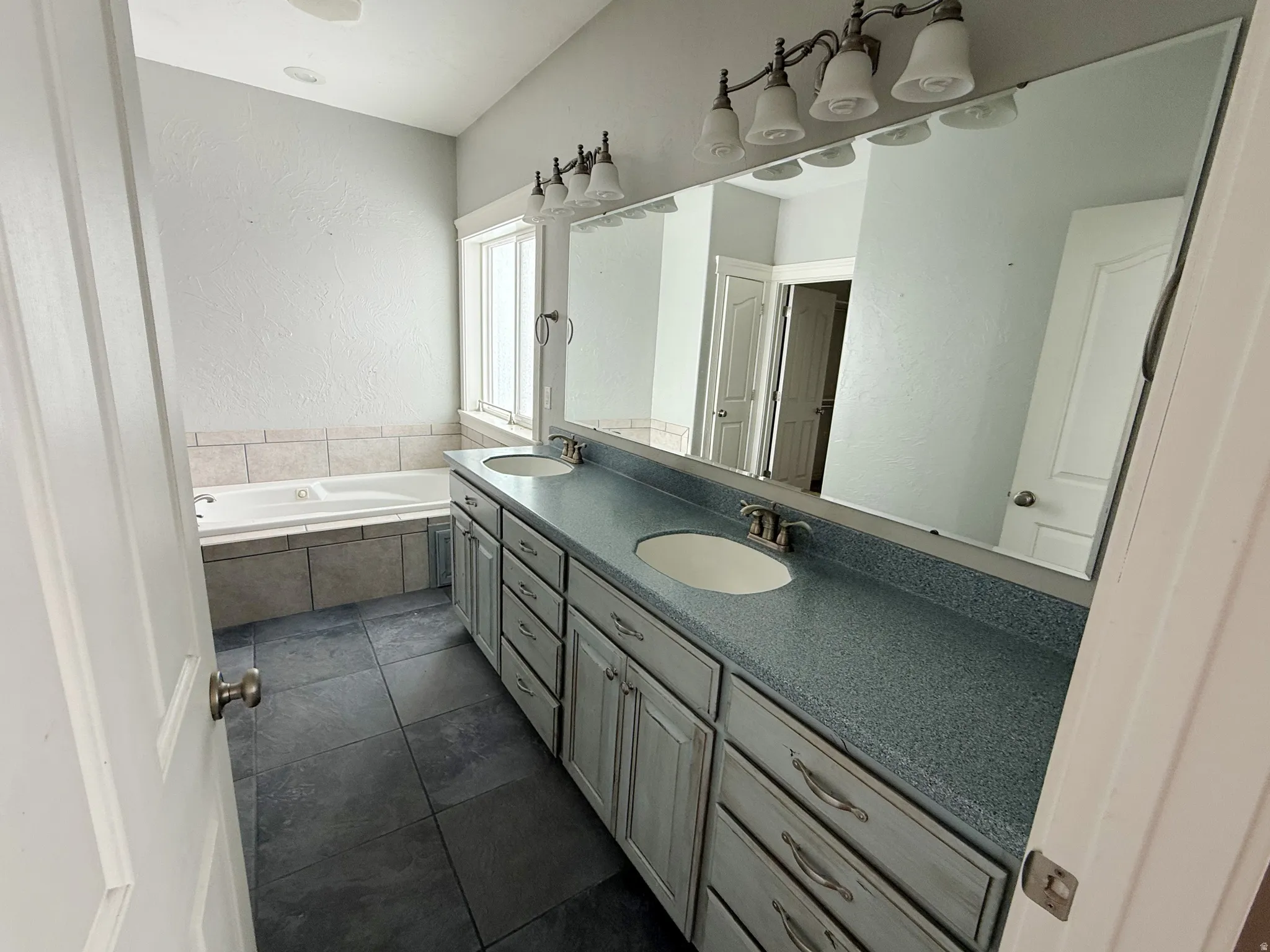 Bathroom featuring double vanity, a textured wall, a garden tub, and dark tile patterned flooring
