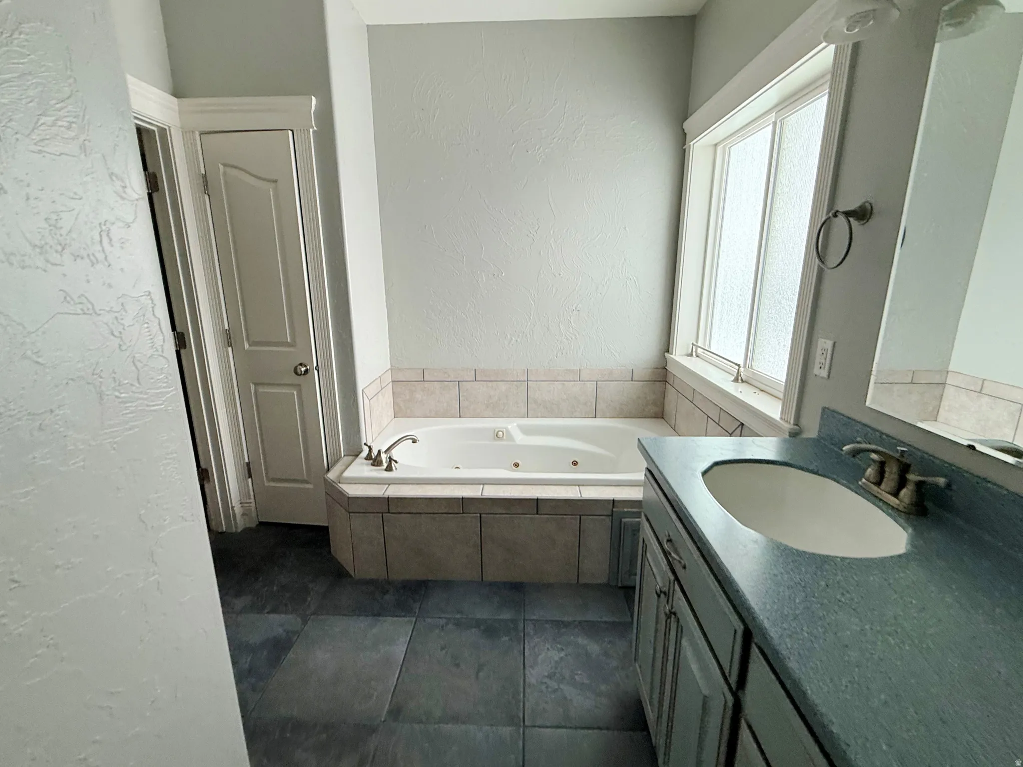 Bathroom with a textured wall, vanity, a whirlpool tub, and dark tile patterned floors