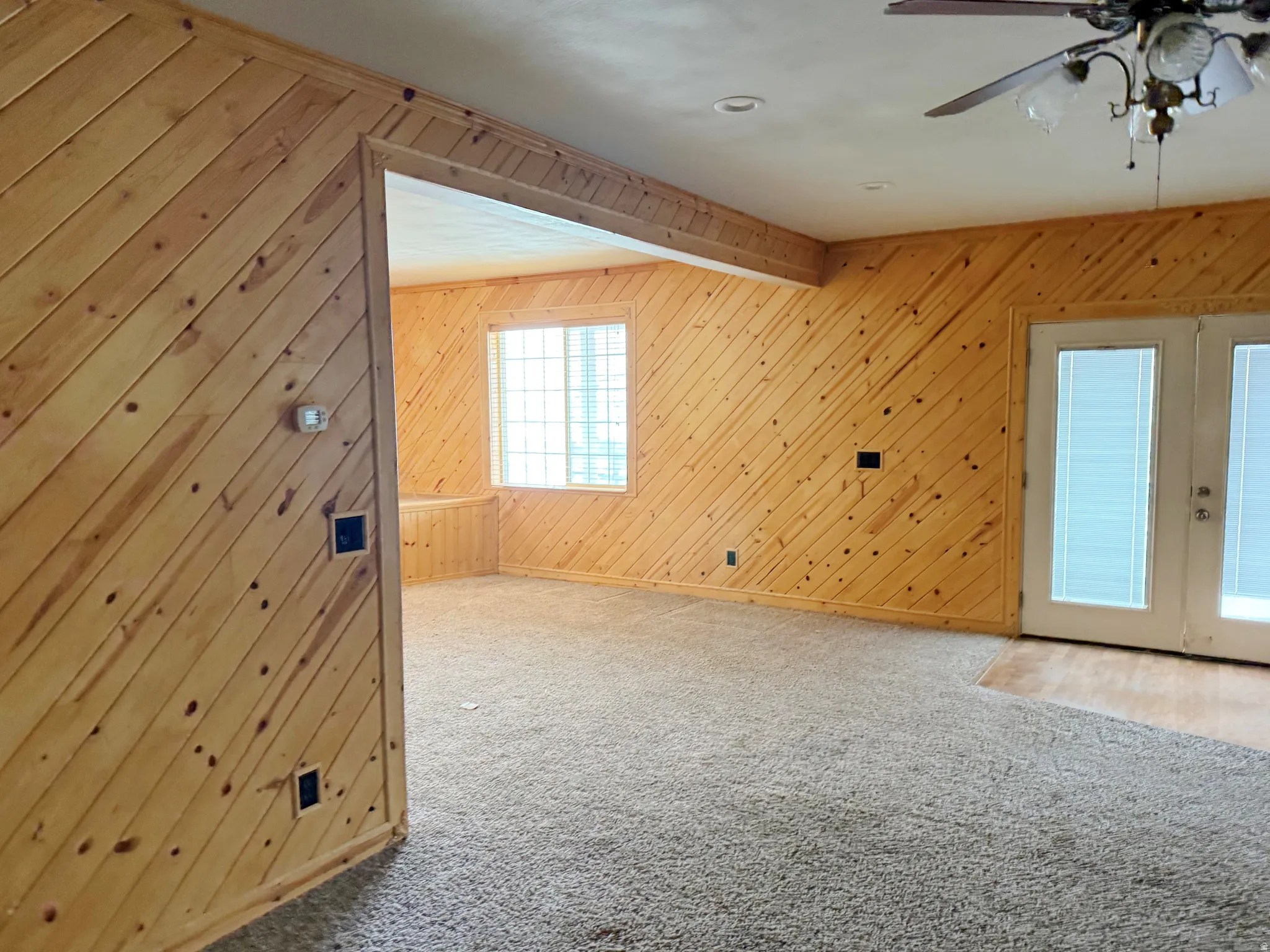 Bonus room featuring a ceiling fan, carpet, wood walls, and french doors