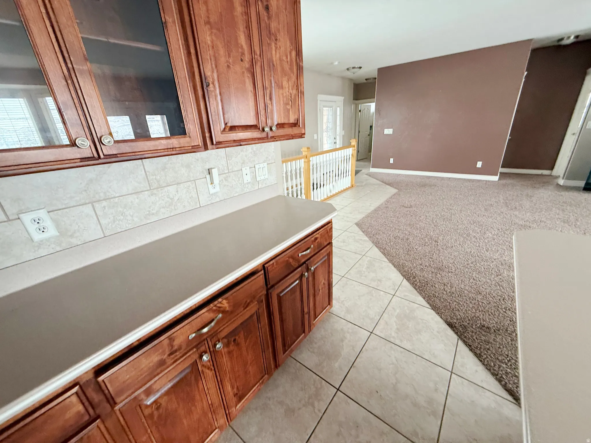 Kitchen featuring light carpet, light tile patterned floors, wood finish cabinetry, glass fronted cabinets, and light countertops