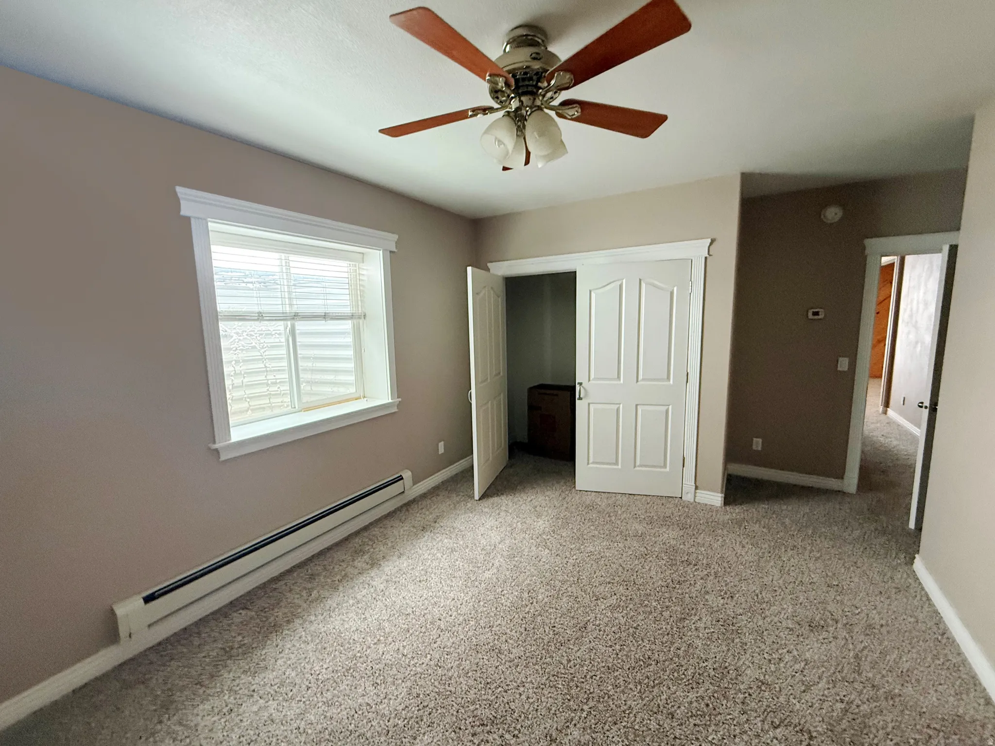 Unfurnished bedroom featuring a baseboard heating unit, light colored carpet, and ceiling fan