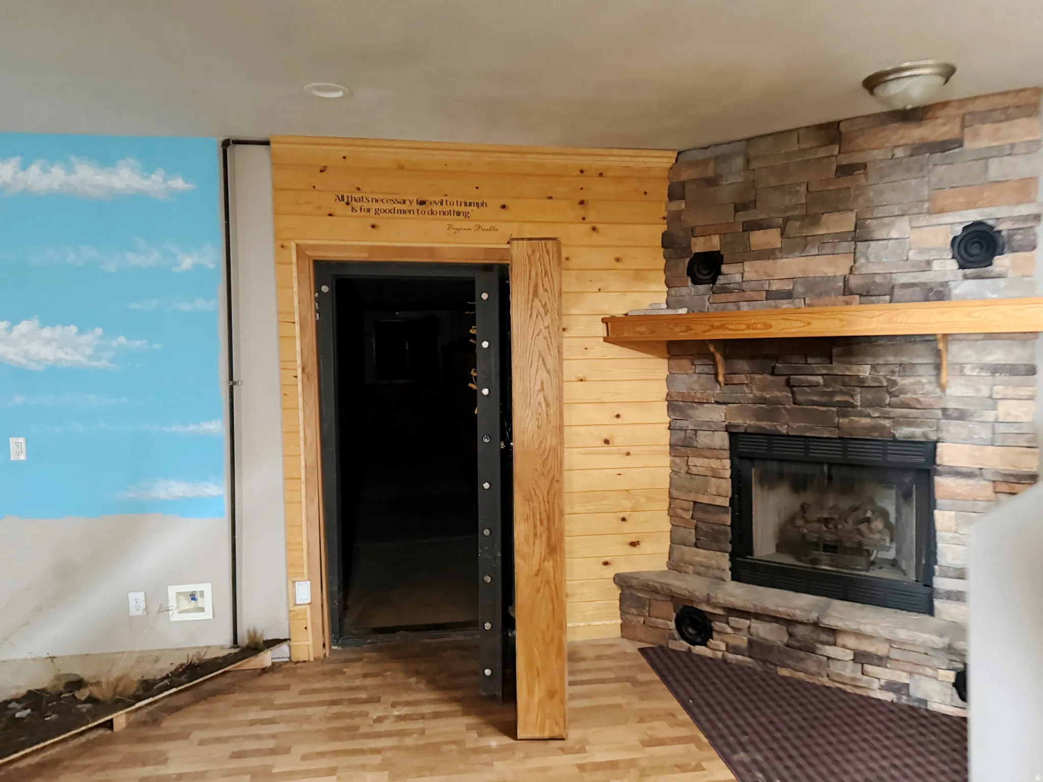 Unfurnished living room with light wood finished floors, a stone fireplace, and wooden walls